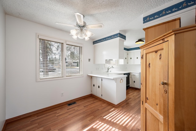 kitchen with light wood finished floors, a peninsula, light countertops, a textured ceiling, and a sink