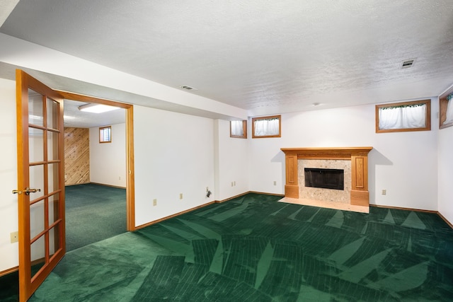 basement featuring visible vents, a fireplace with flush hearth, carpet flooring, a textured ceiling, and baseboards