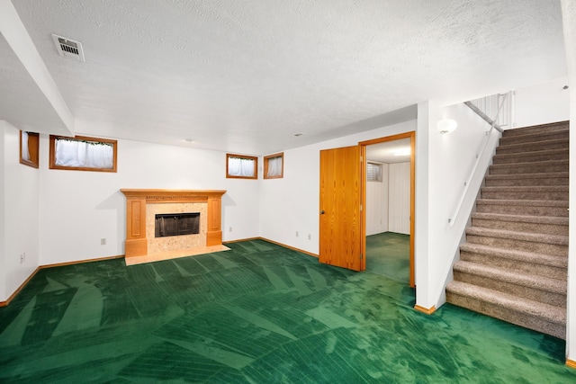 below grade area featuring visible vents, a fireplace with flush hearth, carpet, stairs, and a textured ceiling