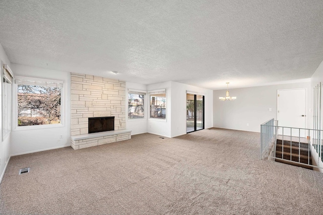 unfurnished living room with a wealth of natural light, carpet flooring, a stone fireplace, and an inviting chandelier