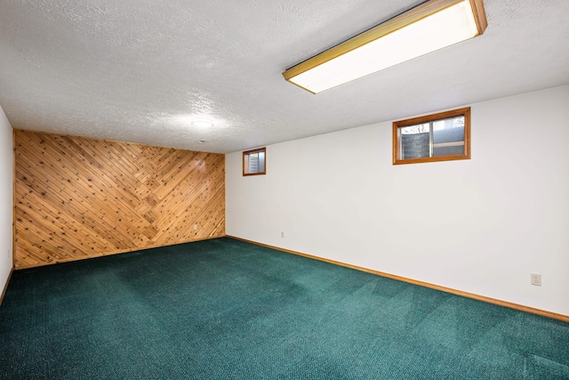 carpeted empty room featuring a textured ceiling, wood walls, and baseboards