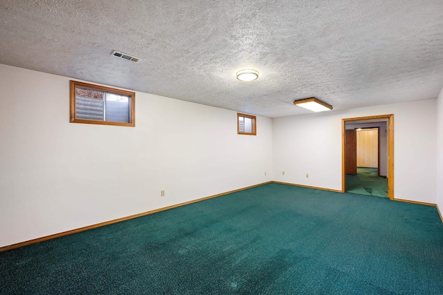 basement featuring a textured ceiling, carpet flooring, visible vents, and baseboards