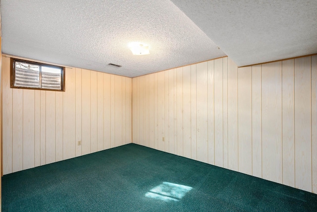 below grade area featuring wood walls, a textured ceiling, visible vents, and carpet flooring