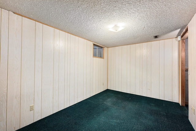 finished basement featuring wood walls, visible vents, dark carpet, and a textured ceiling