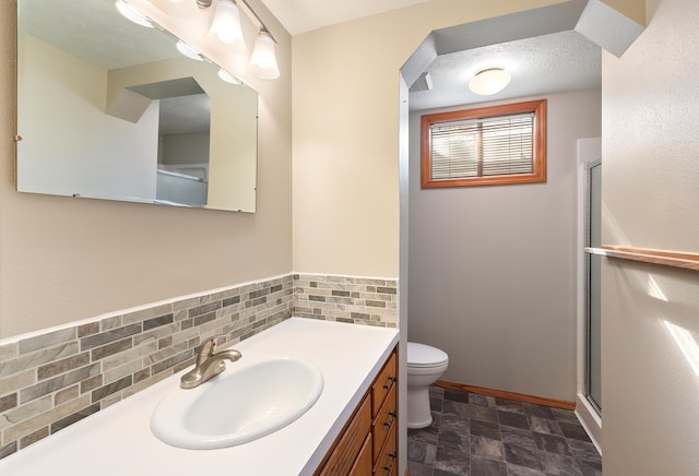 bathroom featuring toilet, stone finish flooring, a shower with shower door, vanity, and a textured ceiling