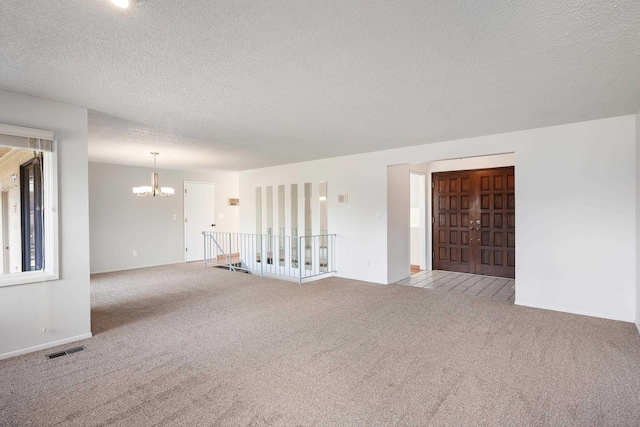 spare room with a textured ceiling, carpet flooring, visible vents, and a notable chandelier