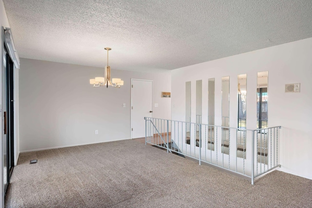 carpeted empty room featuring a textured ceiling and a notable chandelier