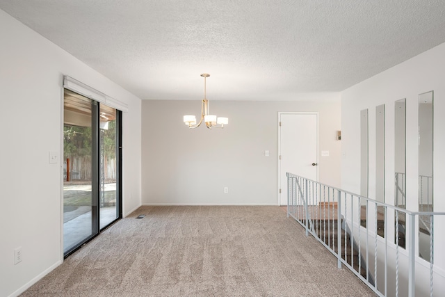 carpeted spare room featuring a textured ceiling, baseboards, and an inviting chandelier