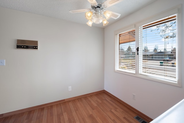 empty room with visible vents, light wood-style floors, a ceiling fan, a textured ceiling, and baseboards