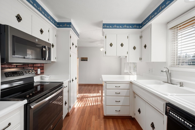 kitchen with light wood finished floors, stainless steel appliances, light countertops, white cabinetry, and a sink