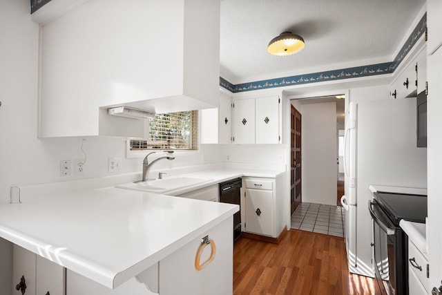 kitchen featuring a peninsula, a sink, white cabinetry, light countertops, and black appliances