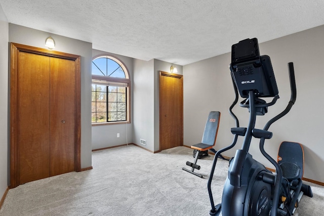 exercise room featuring light carpet, a textured ceiling, visible vents, and baseboards