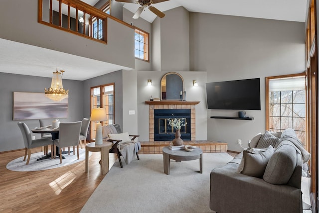 living room featuring a towering ceiling, wood finished floors, a tile fireplace, baseboards, and ceiling fan with notable chandelier