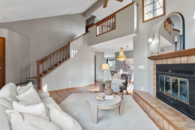 living area with a high ceiling, wood finished floors, visible vents, stairs, and a tiled fireplace