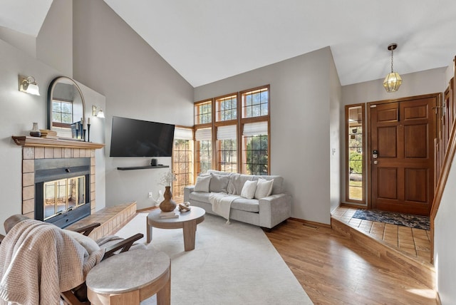 living room featuring a fireplace, an inviting chandelier, wood finished floors, high vaulted ceiling, and baseboards