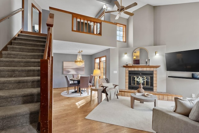 living room with ceiling fan with notable chandelier, wood finished floors, stairway, and a tile fireplace