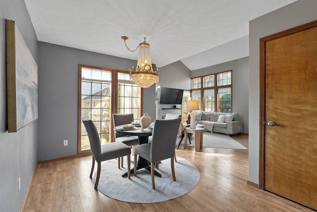 dining area featuring a chandelier, a textured ceiling, lofted ceiling, wood finished floors, and baseboards