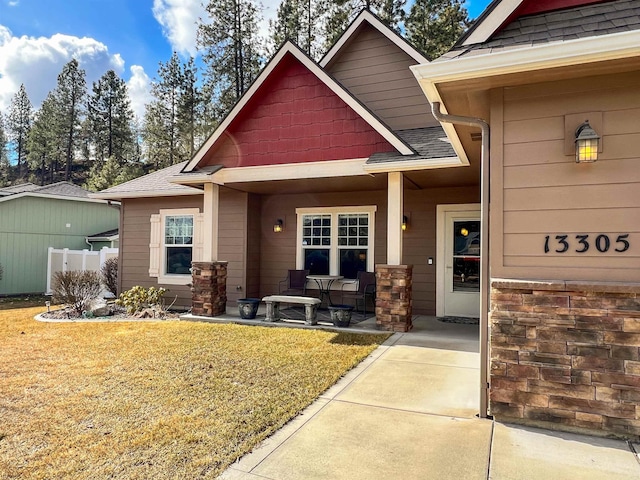 property entrance with a shingled roof, a lawn, and a porch