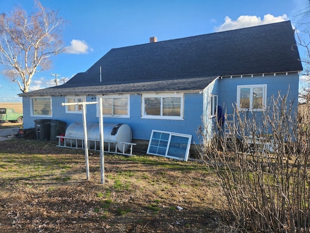 rear view of house featuring a shingled roof and a chimney