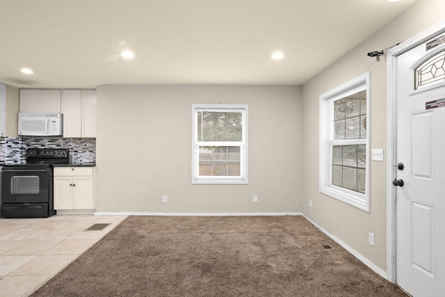 kitchen featuring tasteful backsplash, light colored carpet, black electric range oven, white microwave, and a healthy amount of sunlight