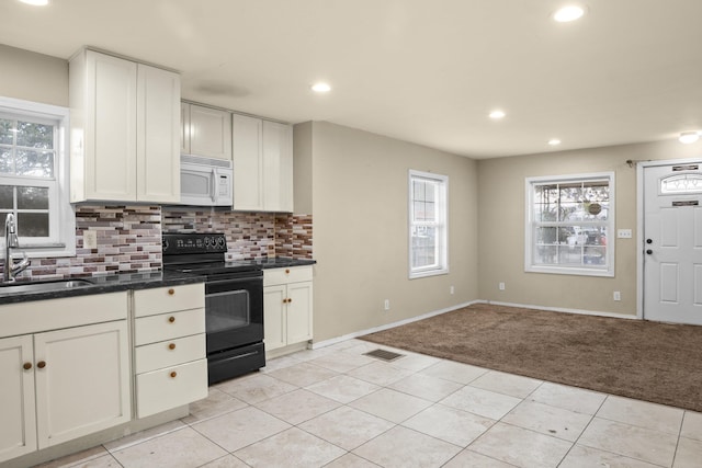 kitchen with visible vents, light colored carpet, white microwave, black range with electric cooktop, and a sink