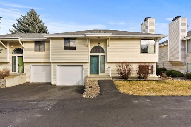 bi-level home featuring driveway, a chimney, an attached garage, and roof with shingles