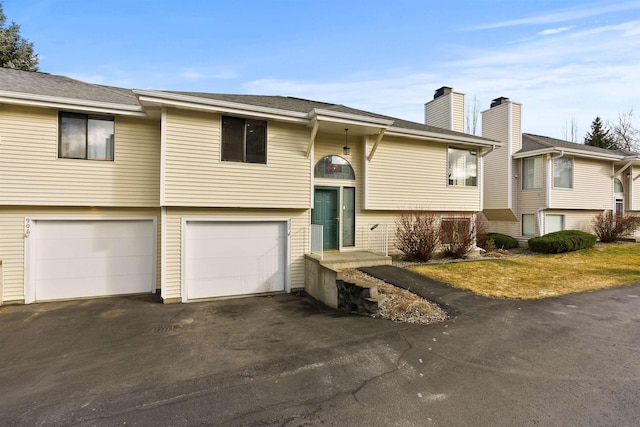 raised ranch with a garage, aphalt driveway, and a chimney