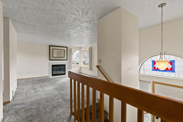 corridor featuring carpet, baseboards, a textured ceiling, and an upstairs landing