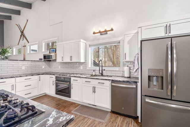 kitchen with decorative backsplash, appliances with stainless steel finishes, white cabinetry, a sink, and dark stone countertops