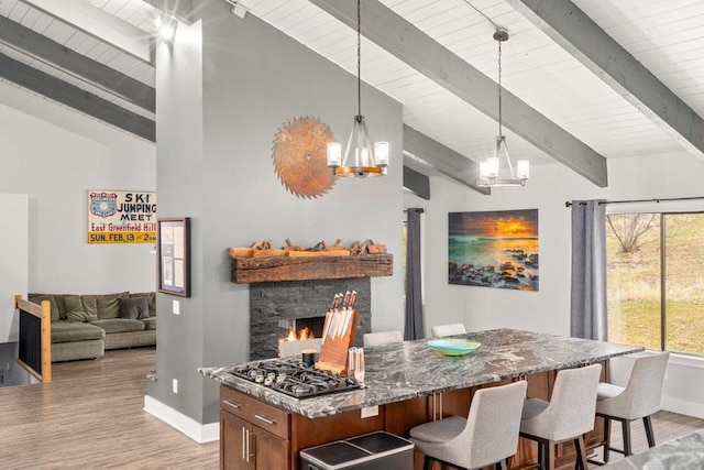 kitchen featuring a chandelier, a breakfast bar area, light wood-style flooring, a fireplace, and dark stone countertops