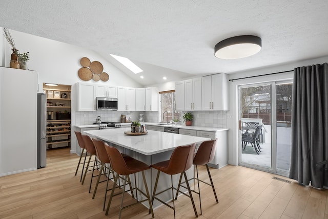 kitchen featuring decorative backsplash, lofted ceiling with skylight, light wood-style flooring, appliances with stainless steel finishes, and a breakfast bar area