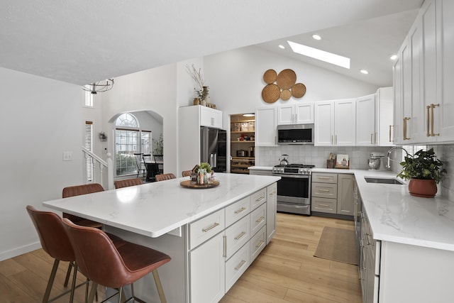 kitchen with a skylight, stainless steel appliances, a sink, a kitchen island, and a kitchen bar