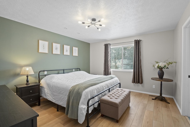 bedroom with a textured ceiling, light wood finished floors, a notable chandelier, and baseboards