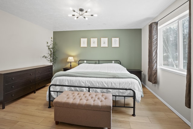 bedroom with light wood-style floors, a notable chandelier, and baseboards