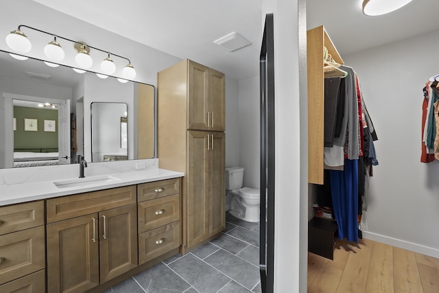 full bathroom with baseboards, toilet, wood finished floors, a walk in closet, and vanity