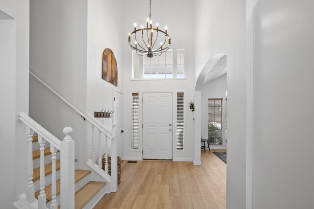 entrance foyer featuring arched walkways, a notable chandelier, a towering ceiling, stairway, and light wood finished floors