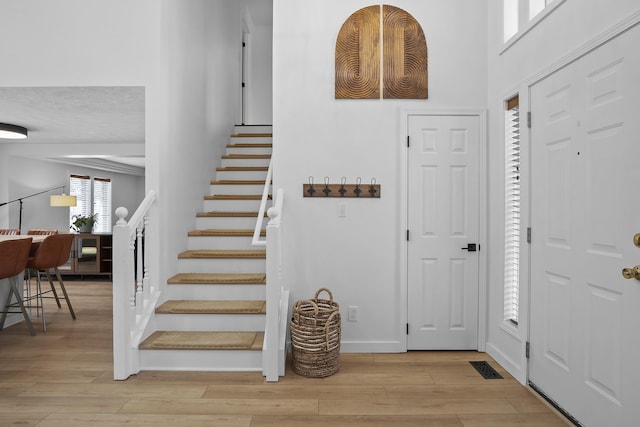 foyer entrance with visible vents, light wood-style flooring, baseboards, and stairs