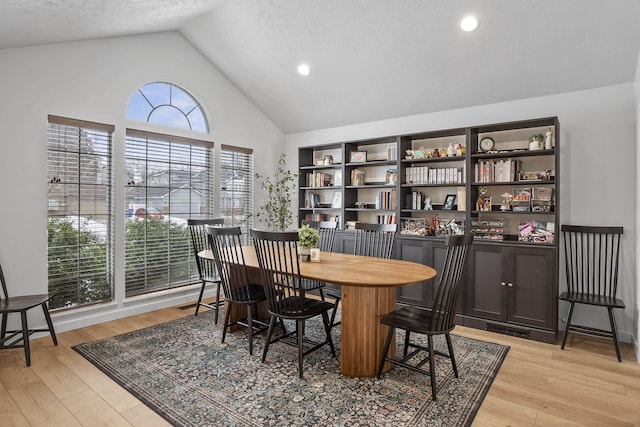 dining room with high vaulted ceiling, light wood-style flooring, and a textured ceiling