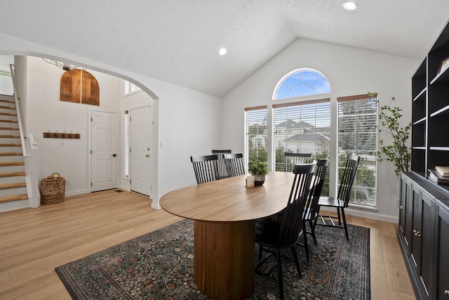 dining space featuring light wood-type flooring, arched walkways, high vaulted ceiling, and stairs