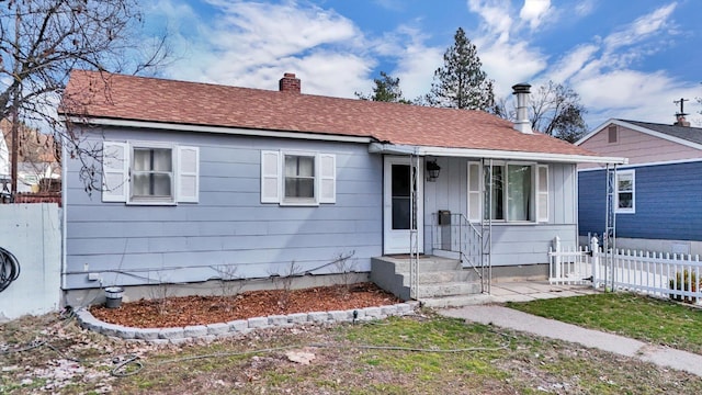 view of front of property with roof with shingles, a chimney, and fence