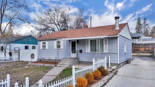 bungalow-style home featuring board and batten siding, a fenced front yard, a chimney, and a shingled roof