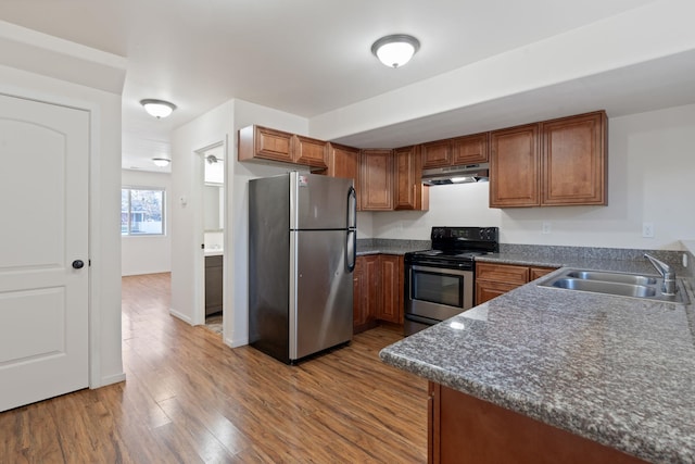 kitchen featuring appliances with stainless steel finishes, brown cabinets, wood finished floors, under cabinet range hood, and a sink