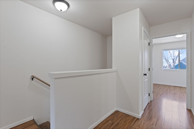 hallway featuring baseboards, wood finished floors, and an upstairs landing