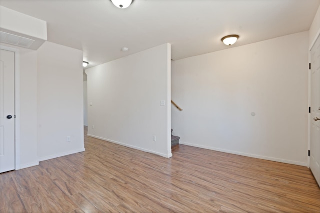 spare room featuring stairs, baseboards, and light wood-style floors