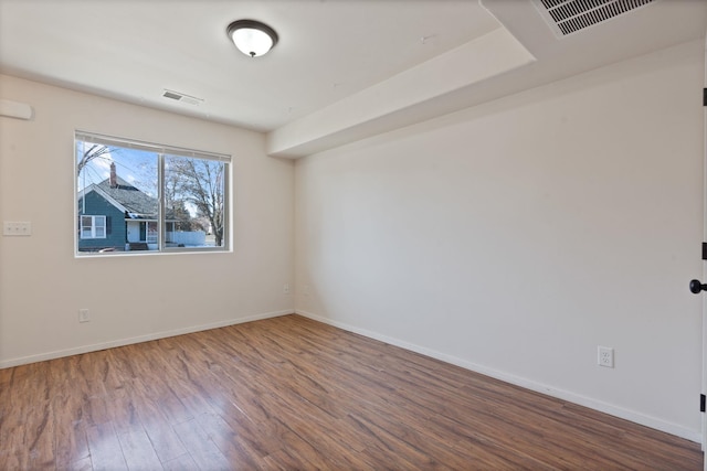 spare room featuring wood finished floors, visible vents, and baseboards