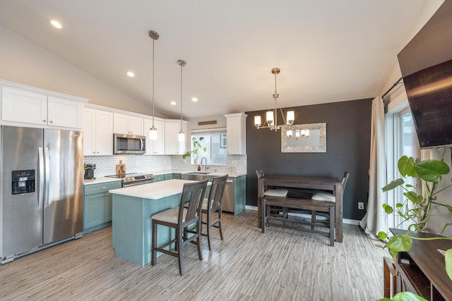 kitchen with vaulted ceiling, stainless steel appliances, light countertops, white cabinetry, and backsplash