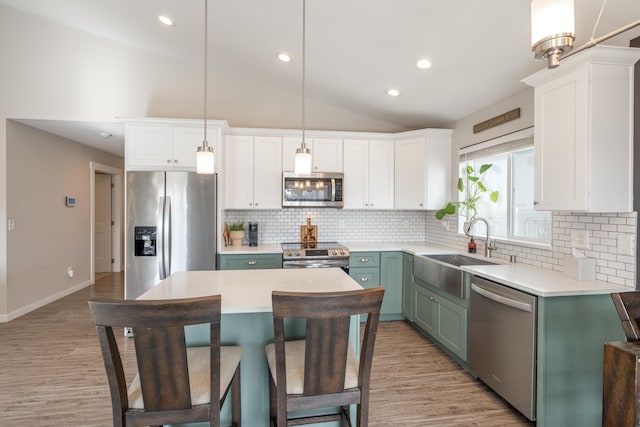 kitchen with a center island, stainless steel appliances, lofted ceiling, white cabinetry, and a sink