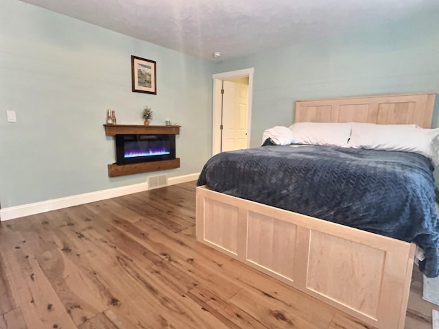 bedroom with a glass covered fireplace, visible vents, baseboards, and wood finished floors