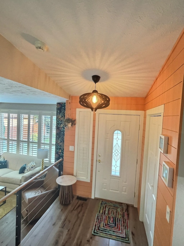 foyer entrance featuring a textured ceiling, wooden walls, vaulted ceiling, and wood finished floors