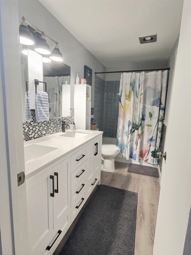 full bathroom featuring double vanity, tasteful backsplash, toilet, wood finished floors, and a sink